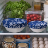 Two white bowls with blue floral lids on a kitchen shelf with vegetables and eggs.