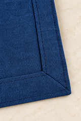 Close-up of the reverse of a navy linen napkin, showing its 2.5cm double-fold hem, matching stitching and mitred corner.