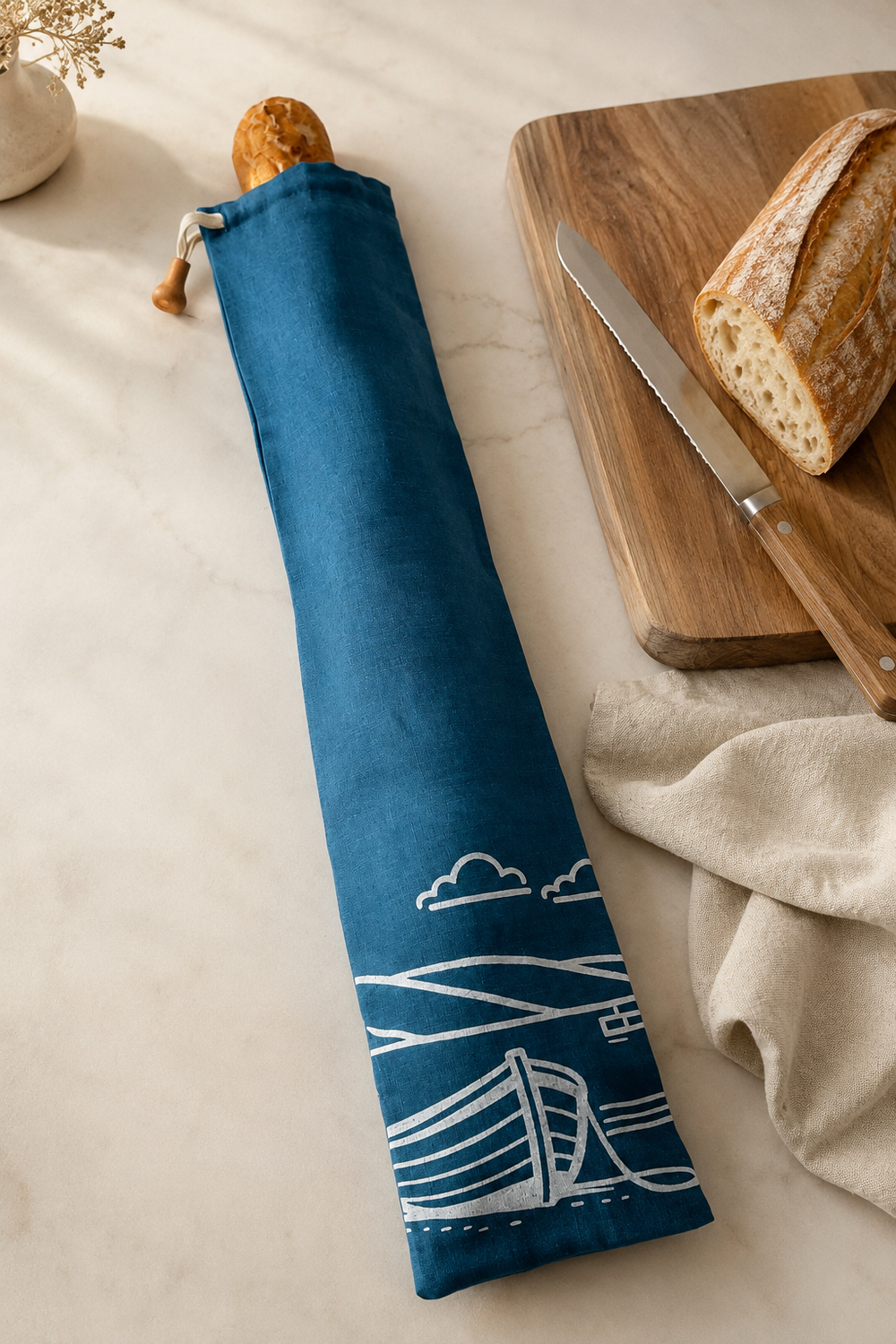 A slim, reusable linen baguette bag in navy, hand printed with the Fjære coastal design in white. Made in Derbyshire for carrying and storing French sticks, artisan baguettes and long crusty loaves.
