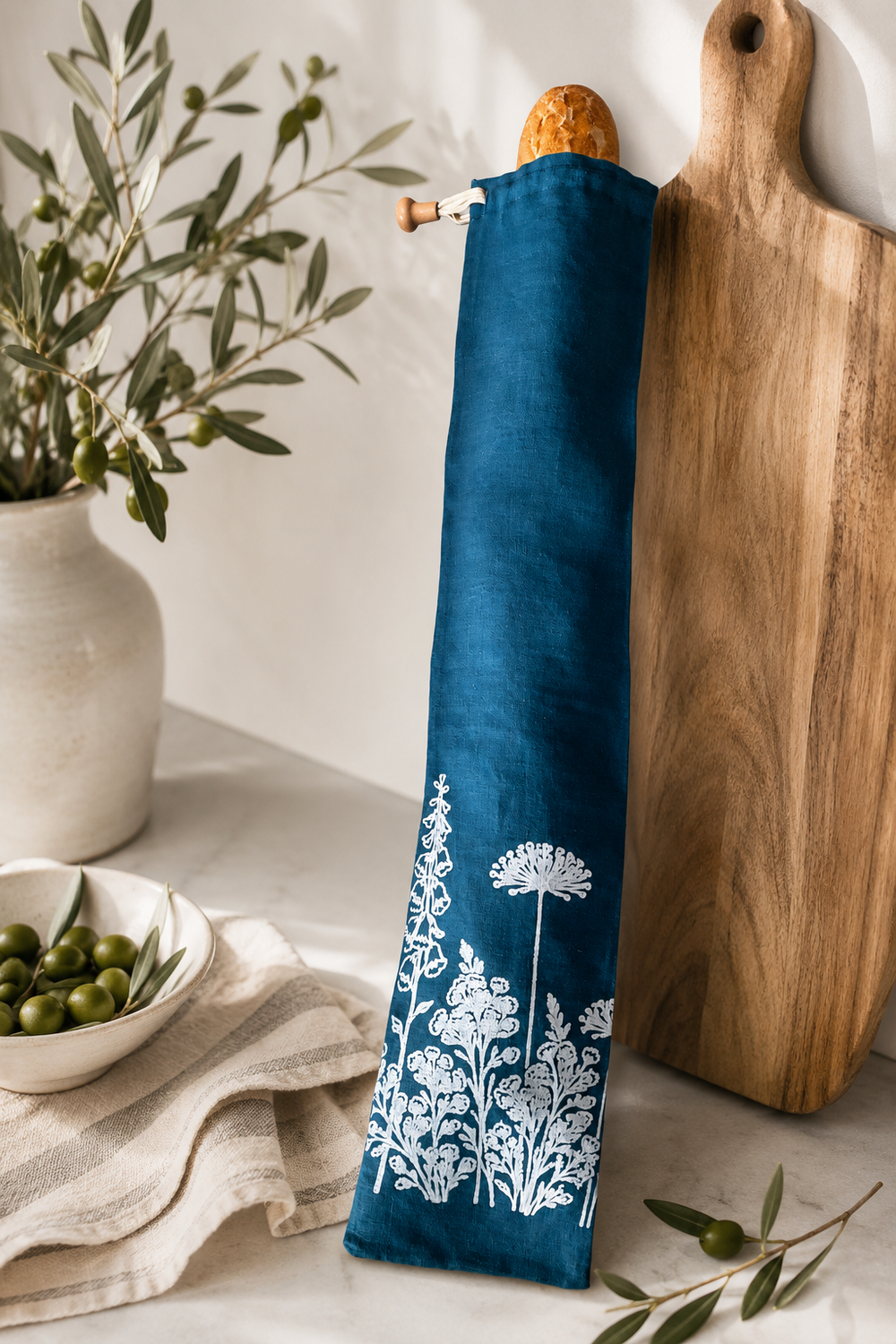 A reusable linen baguette bag in deep navy, hand printed with the Florilegium floral design in white. Made for carrying and storing French sticks, artisan baguettes and crusty bread without folding or squashing the loaf. Breathable, washable and plastic-free.