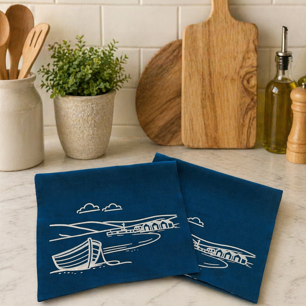 Blue linen tea towels with white coastal designs hand printed set on a kitchen counter.