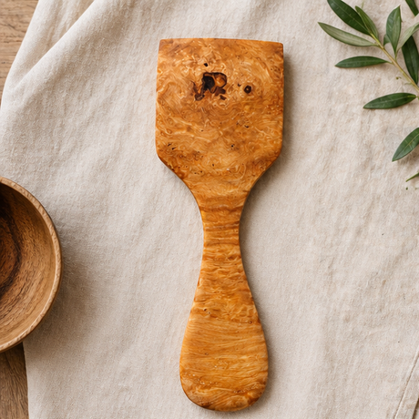 Wooden spatula on a light fabric background with a bowl and leaves.