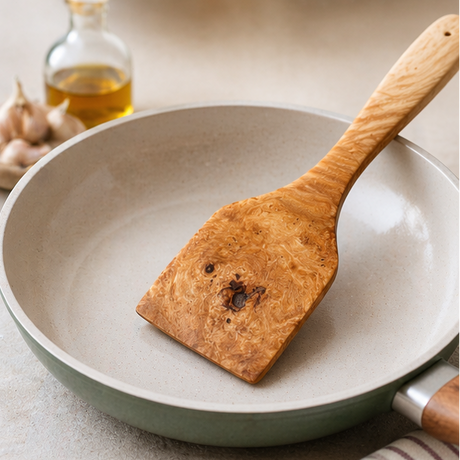 Wooden spatula in a ceramic frying pan with garlic and oil in the background