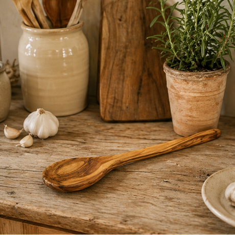 Wooden spoon on a wooden surface with a potted plant and garlic in the background.