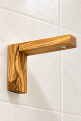 Angled view of an olive wood soap holder showing the adhesive backing and removable metal disc.
