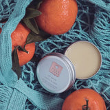 tin of lip balm on a blue textured surface with oranges and leaves.