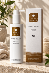 Pure Lakes Hand Wash bottle and packaging box in Orange & Neroli scent, styled on a stone surface with soft natural lighting and decorative leaves.