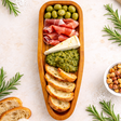 Wooden platter with cured meats, olives, cheese, and bread on a light background.