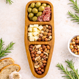 Wooden snack tray with olives, cheese, salami, and nuts on a light surface with rosemary.
