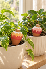 Set of two Ana Rose ceramic watering spikes with tapered terracotta bodies, rounded patterned tops and cork stoppers. Two coordinating scalloped designs feature blush pink, red, ochre and cream