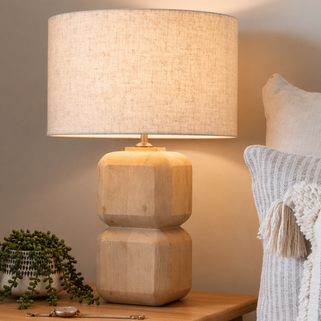 Wooden side table with a lamp and plant next to a cozy sofa with pillows.