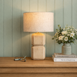 Wooden lamp on a wooden surface with books and flowers against a green paneled wall.