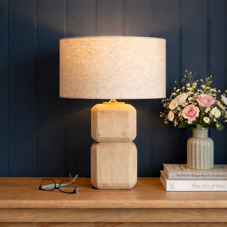 Beige lamp with a textured shade on a wooden surface against a dark blue wall.
