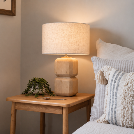 Wooden side table with a lamp and plant next to a cozy sofa with pillows.
