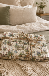 A gift-wrapped box with Personalised Chicken Wrapping Paper  tied with twine sits on a bed with neutral-toned bedding and pillows in a softly styled bedroom setting.
