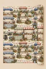 A roll of Personalised Country Show Wrapping Paper, shown partially unrolled on a solid beige background. The pattern depicts multiple rustic market stalls with red, blue, and green striped awnings, decorated with potted plants, baskets, and colourful bunting flags.