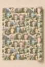 A rolled sheet of wrapping paper or gift wrap featuring a repeating pattern of pastel beach huts with door signs that can be personalised, benches, and garden foliage on a light cream background, shown against a solid beige backdrop.