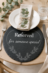 Table setting with a 'Reserved for someone special' placemat, white plate, and greenery.