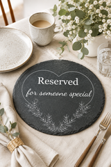 Round slate board with 'Reserved for someone special' text on a table setting with plates, cup, and flowers.