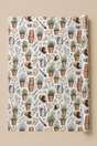 A roll of Personalised Terracotta Pot  wrapping paper featuring a repeating botanical and gardening pattern with potted plants, watering cans, trowels, wooden signs, and lavender sprigs on a white background, shown against a warm beige backdrop.