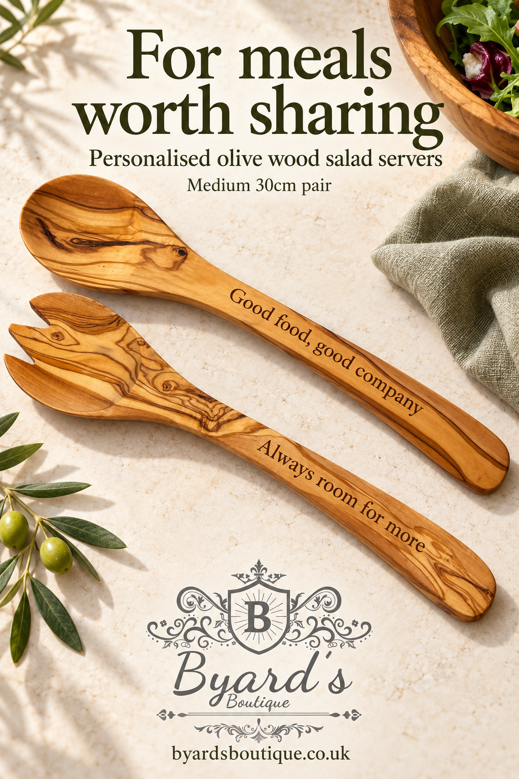 Medium olive wood salad spoon and fork engraved with “Good food, good company” and “Always room for more”, arranged on pale stone beside sage linen.
