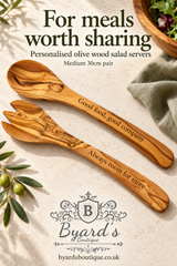 Medium olive wood salad spoon and fork engraved with “Good food, good company” and “Always room for more”, arranged on pale stone beside sage linen.