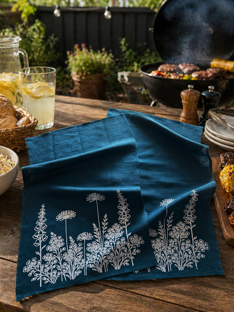 Blue hand printed linen tea towels with floral patterns on a wooden table outdoors.