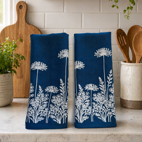 Two blue linen tea towels with white floral patterns on a kitchen counter.