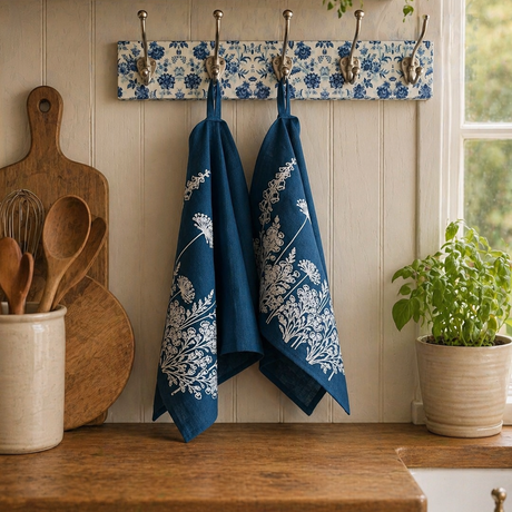 Kitchen scene with blue floral patterned linen tea towels hanging on a hook rack, wooden utensils, and a plant.