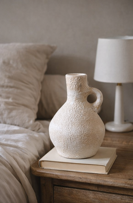 Textured white vase on a stack of books with a lamp in the background