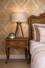 Wooden nightstand with lamp next to a bed with decorative pillows against a patterned wall.