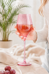 Person holding a pink twist wine glass with a blurred background