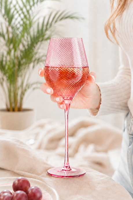 Person holding a pink twist wine glass with a blurred background