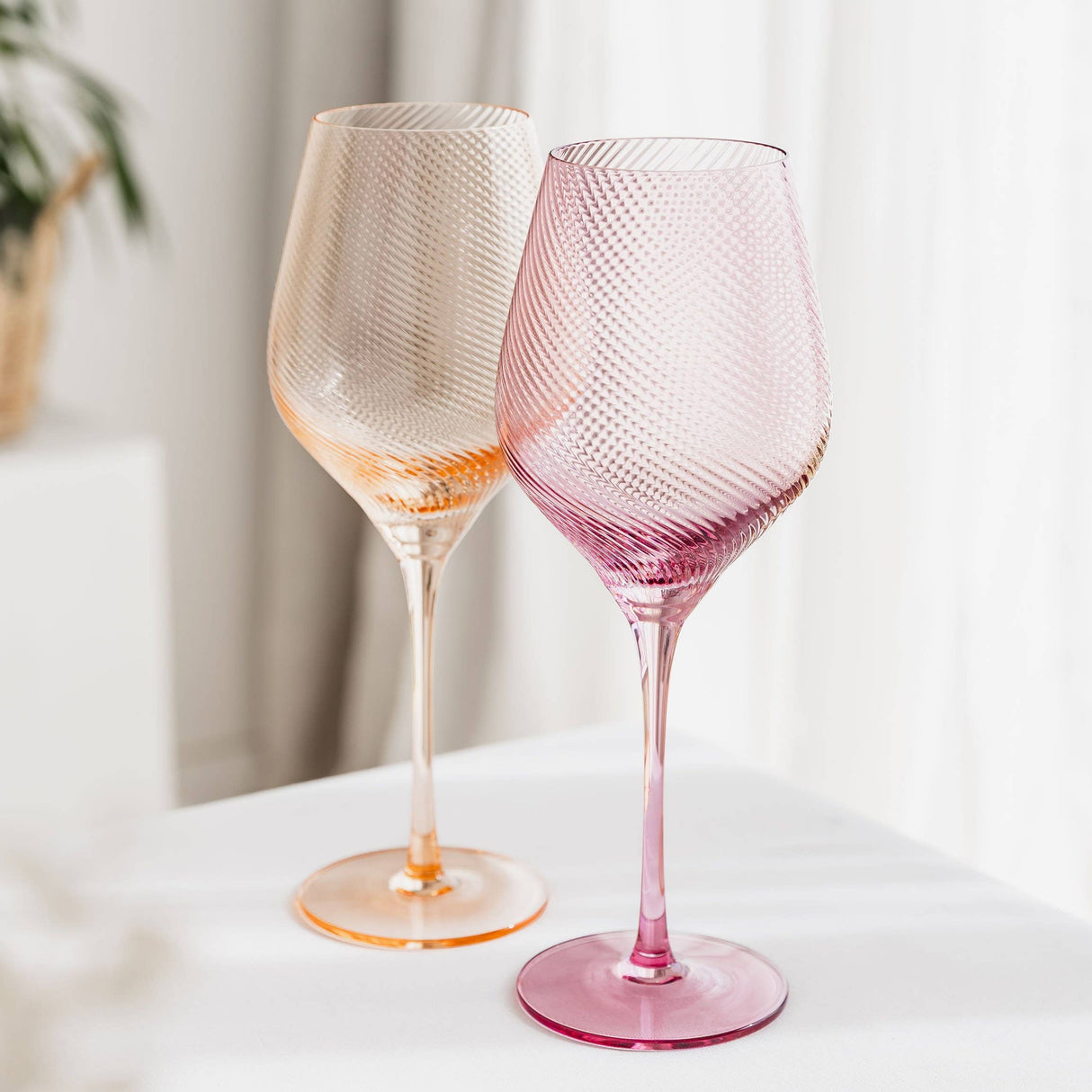 Two textured twist wine glasses, one peach and one pink, on a light surface with a light background.