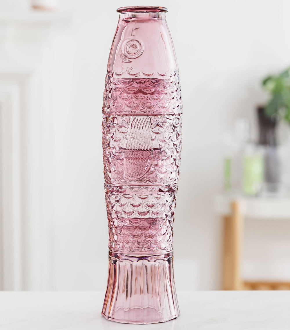 Pink stacking glass set that makes a fish when stacked on a white surface with a blurred background