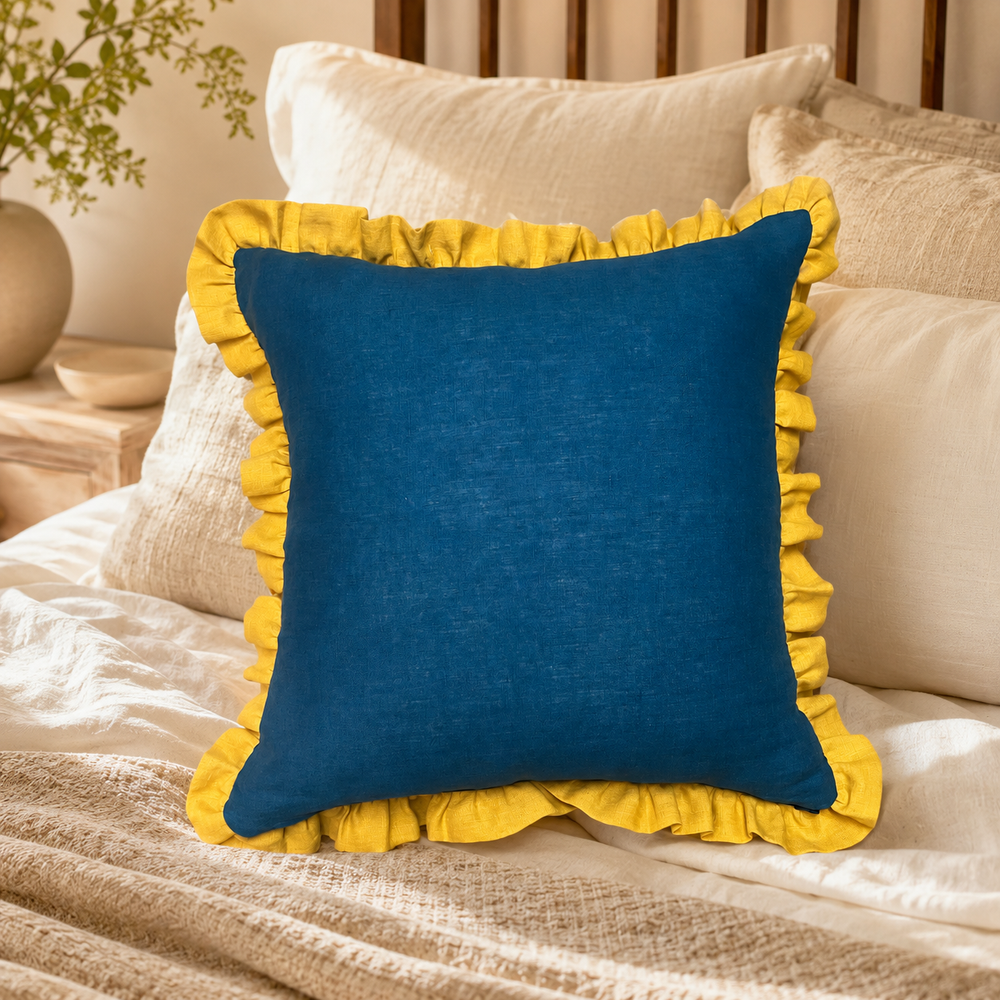 Plain deep blue linen cushion cover with mustard ruffle edge styled on a bed.