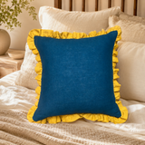 Plain deep blue linen cushion cover with mustard ruffle edge styled on a bed.