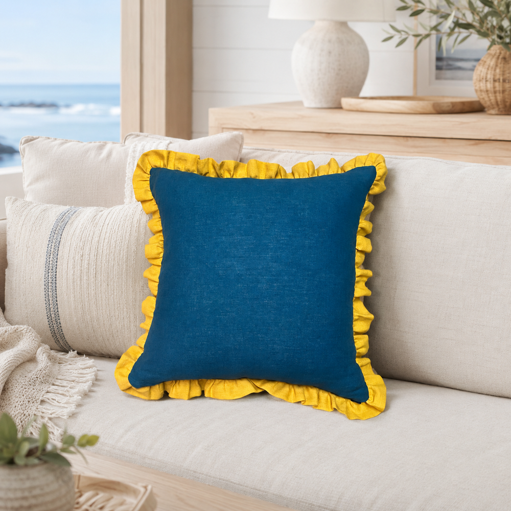 Plain deep blue linen cushion cover with mustard ruffle edge styled on a sofa in a beach house.