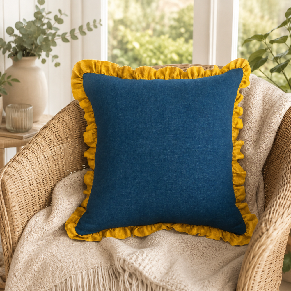 Plain deep blue linen cushion cover with mustard ruffle edge styled on a wicker chair.