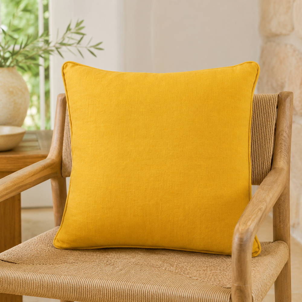 Plain mustard linen cushion cover with piped edge styled on a wicker chair.