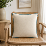 Plain natural linen cushion cover with duck egg piping styled on a wicker chair.