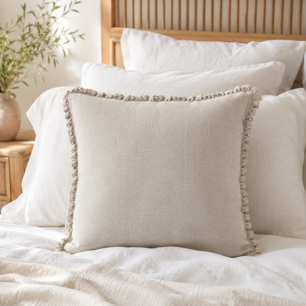 Plain natural linen cushion cover with ruffle edge styled on a bed.