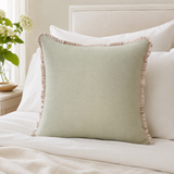 Plain sage linen cushion cover with pale ruffle edge styled on a neutral bed.