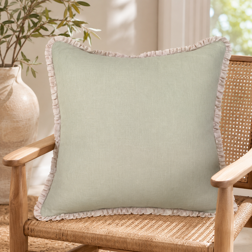 Plain sage linen cushion cover with pale ruffle edge styled on a wicker chair.