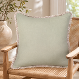 Plain sage linen cushion cover with pale ruffle edge styled on a wicker chair.