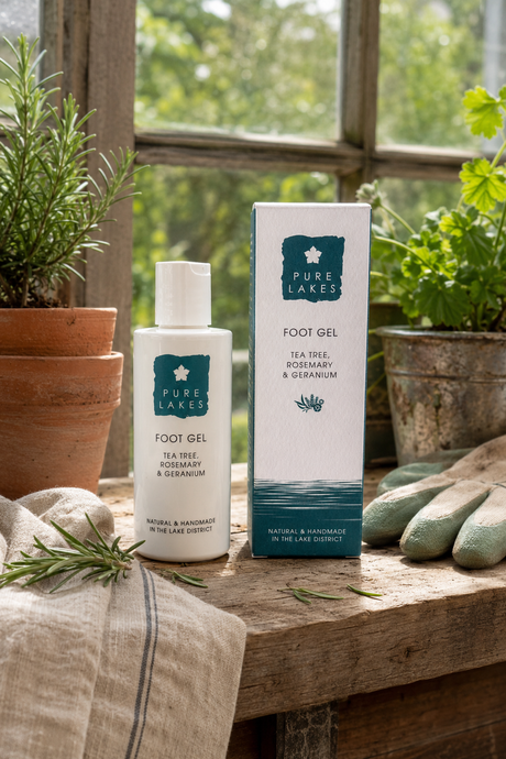 Pure Lakes Foot Gel bottle and matching box displayed on a rustic wooden table in a garden greenhouse setting, surrounded by potted plants and gardening gloves.