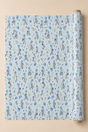 Light blue wrapping paper with a repeating pattern of Power Blue Bonnet Girls Wrapping Paper, shown partially unrolled from a wooden roll against a solid beige background.