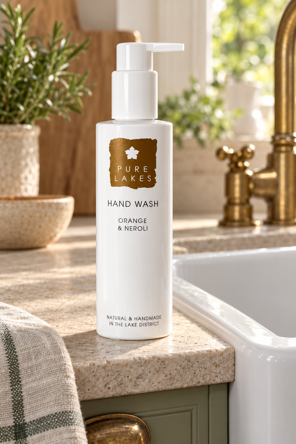 A bottle of Pure Lakes Hand Wash in the Orange & Neroli scent, standing on a speckled kitchen counter next to a sink with a gold faucet.
