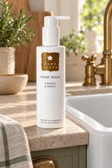 A bottle of Pure Lakes Hand Wash in the Orange & Neroli scent, standing on a speckled kitchen counter next to a sink with a gold faucet.
