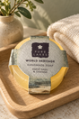 A round bar of Pure Lakes handmade soap labeled 'World Heritage Sweet Basil & Orange' resting on a wooden tray, with a beige towel and a small potted plant in the background.
